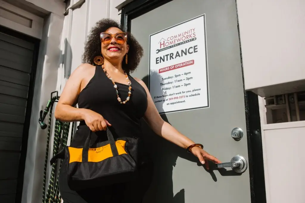 Woman with a yellow tool bag standing in front of a door.