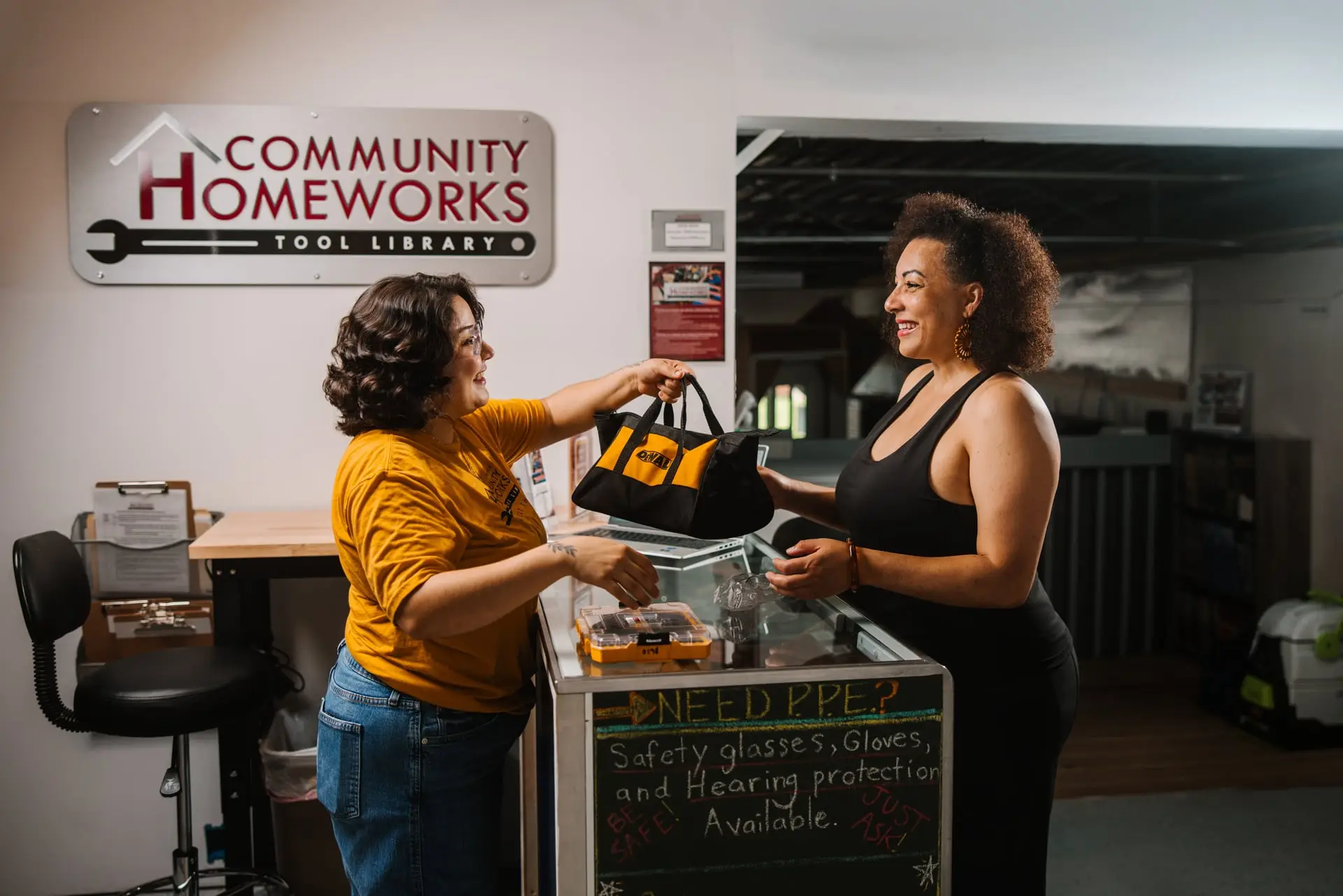 Two woman holding a bag over a counter in the Community Homeworks building.