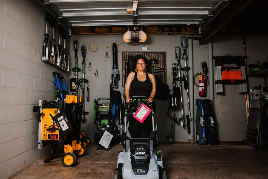 Woman standing behind a lawn mower in a tool garage.