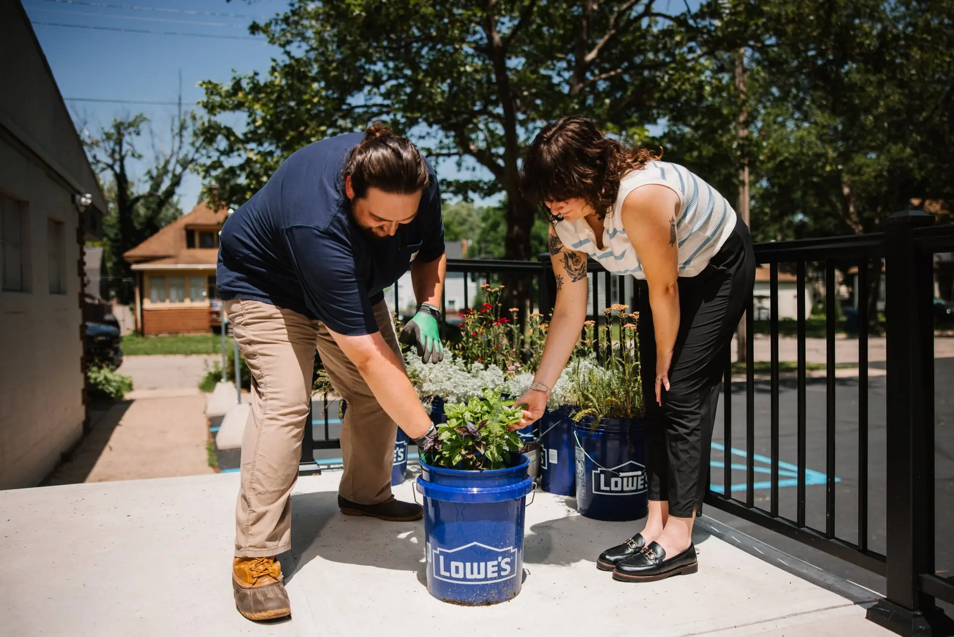 A man and woman pulling weeds out of a blue bucket.