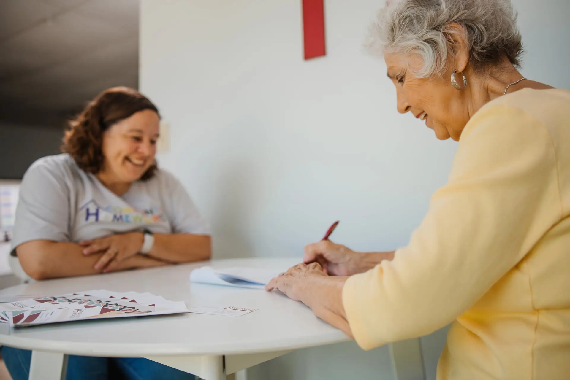 Two woman sitting at a table doing paperwork.
