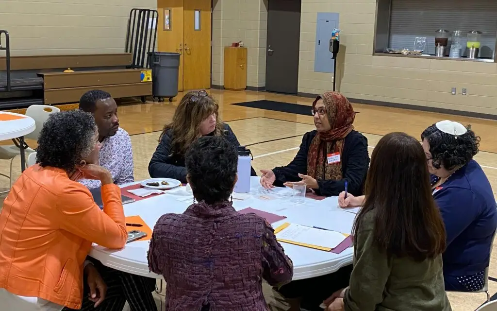 Group of people sitting around a white table at Community Homeworks Faith Based Round Table discussions.