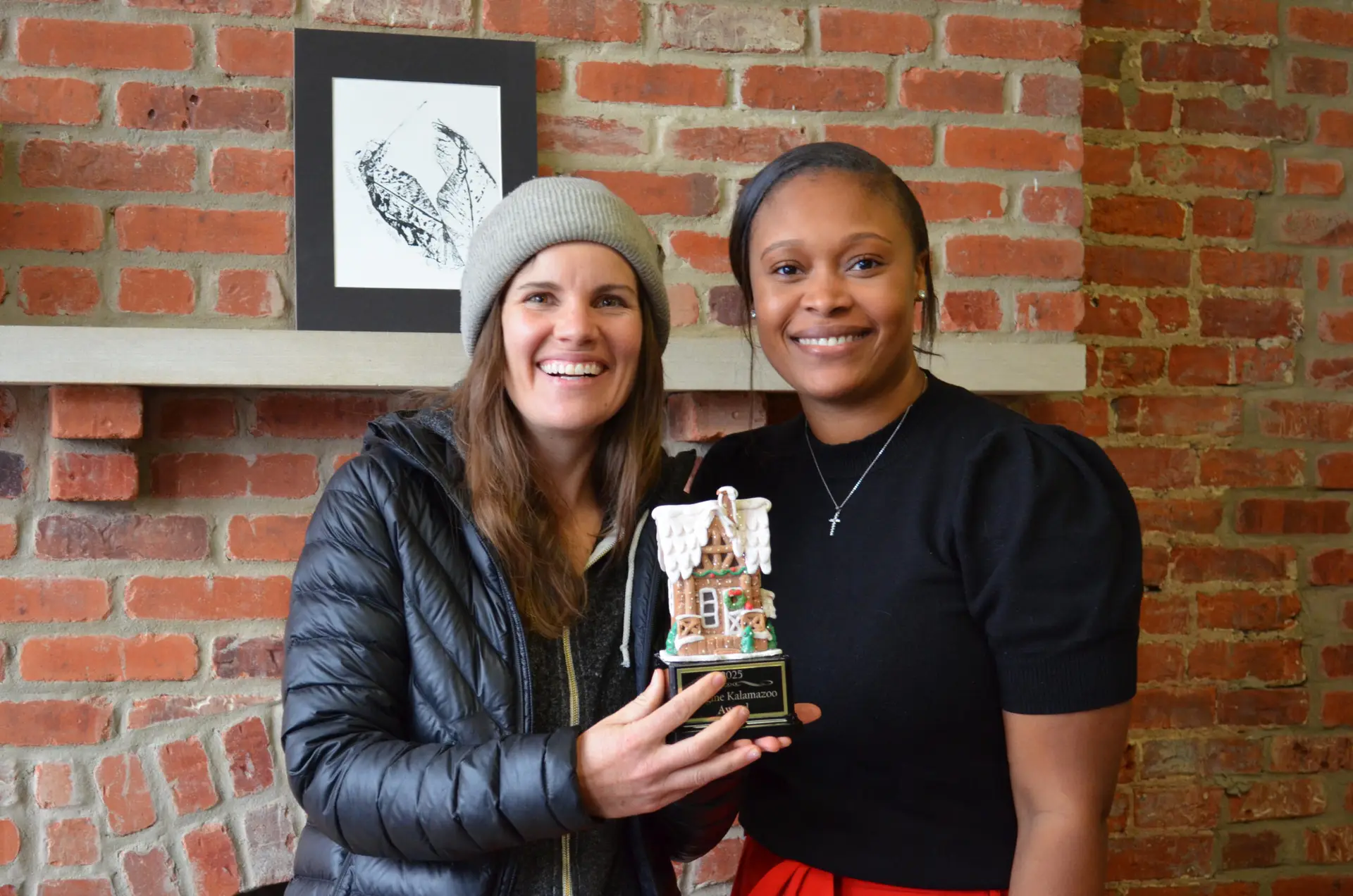 Two woman standing with a GingerBread House Contest trophy.